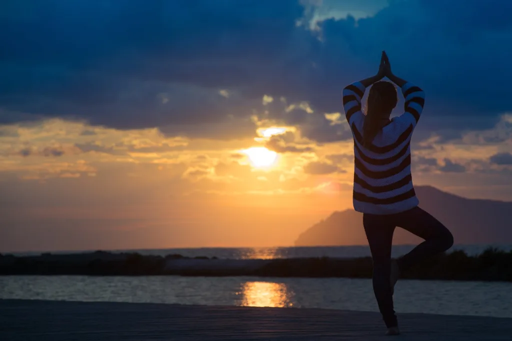 Mulher praticando yoga no por do sol para ter vida plena