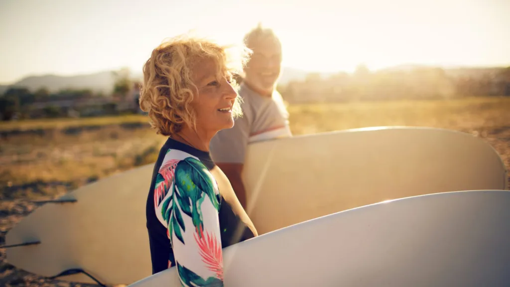 Mulher de meia idade segurando uma prancha de surf conferindo uma boa vida aos 50